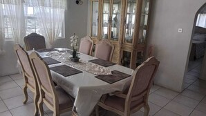 Un coin repas avec une table dressée pour six personnes, entourée de chaises, un buffet avec des portes en verre et une fenêtre avec des rideaux.