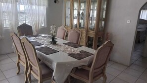 Un comedor con una mesa dispuesta para seis personas, rodeada de sillas, un aparador con puertas de vidrio y una ventana con cortinas.
