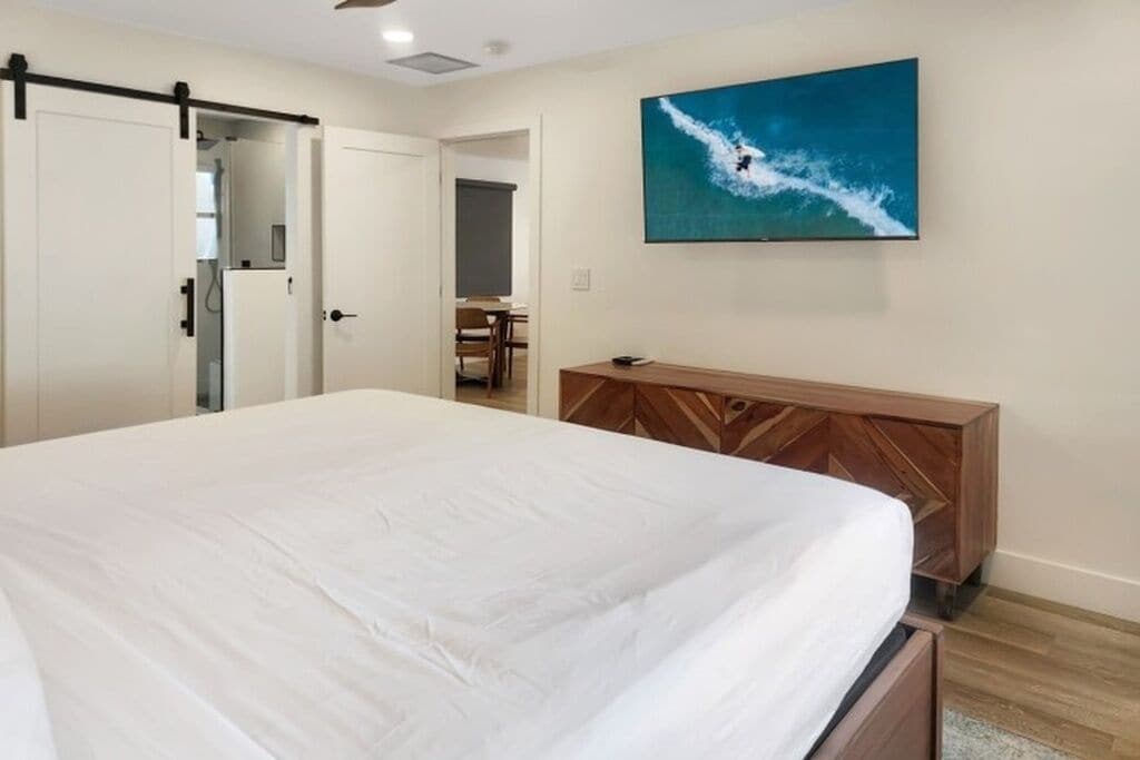 Una camera da letto con un letto, una cassettiera in legno, una porta scorrevole e una TV a parete che mostra un surfista.