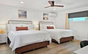 Habitación de hotel con dos camas, ventilador de techo y obras de arte en las paredes.