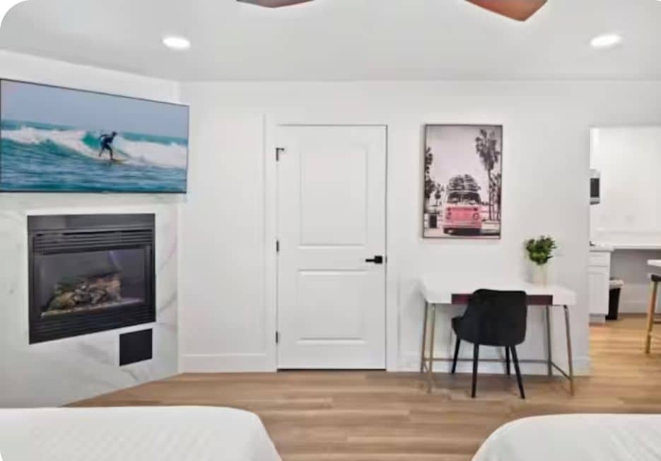 Una habitación con chimenea, un cuadro de un surfista, una puerta y una mesita con una silla.