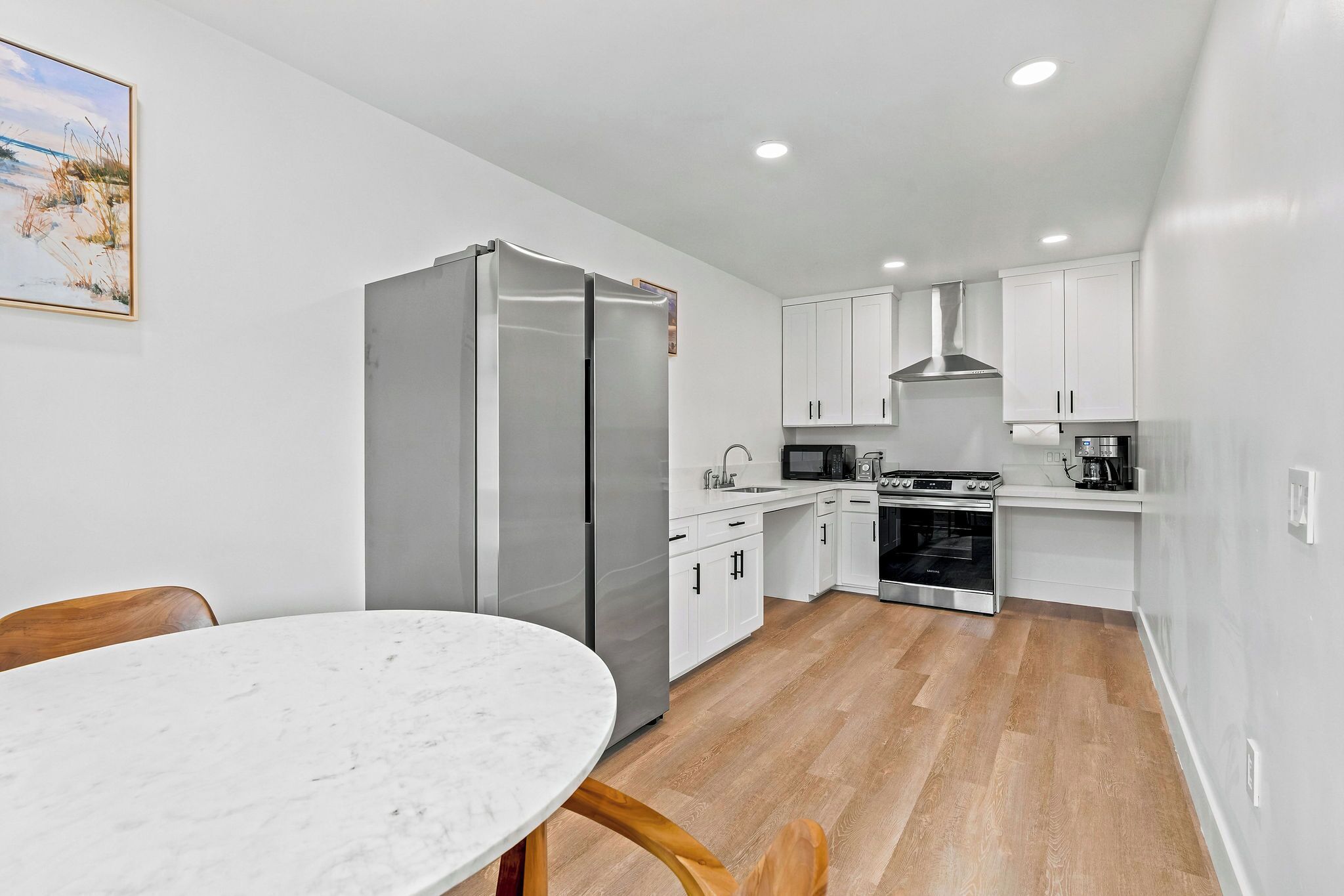 A modern kitchen with white cabinets, a stainless steel refrigerator, a microwave, and an oven.