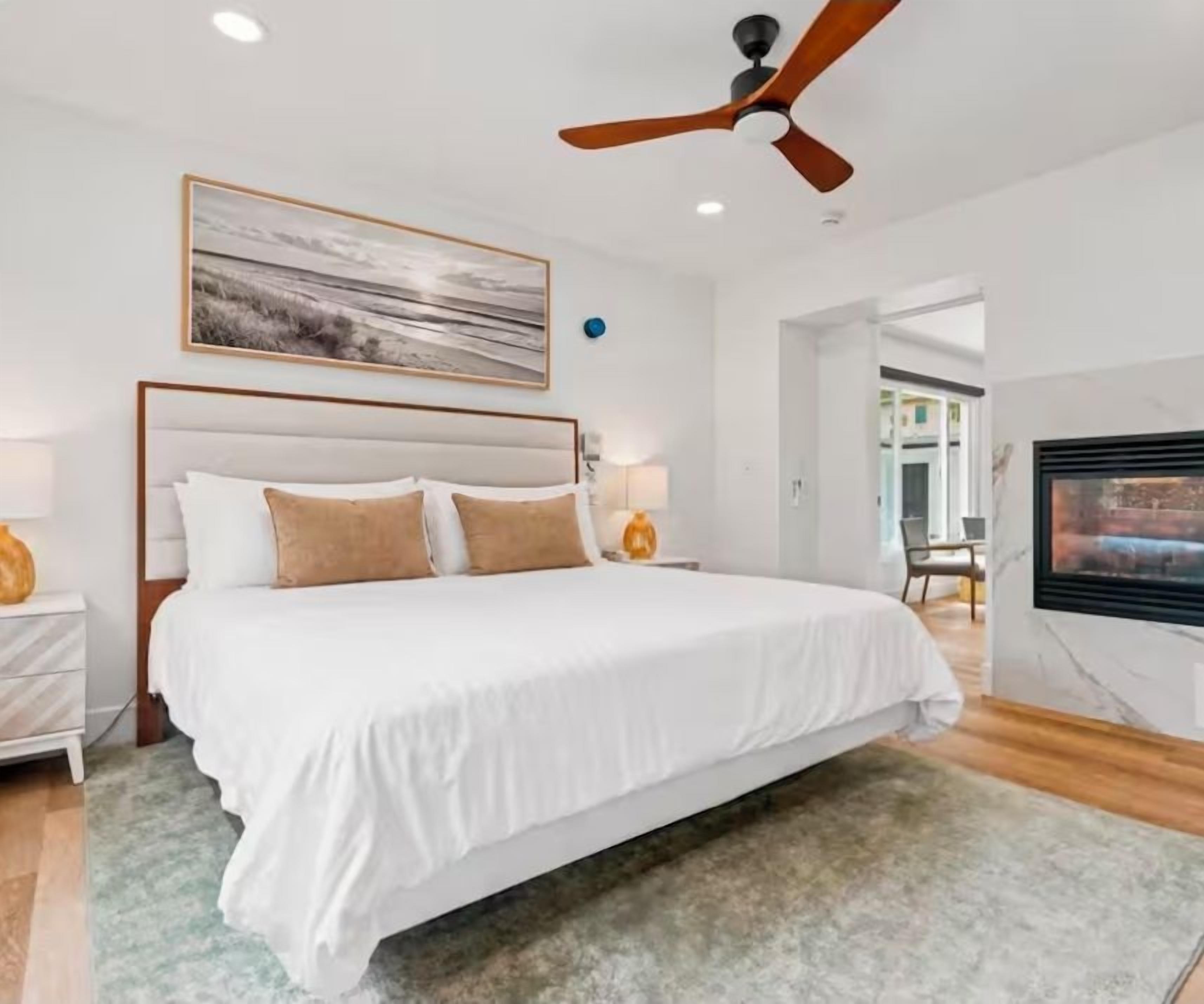 A bedroom with a bed, a ceiling fan, a painting, and a TV.