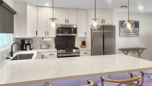 Una cocina moderna con gabinetes blancos, electrodomésticos de acero inoxidable y una isla grande con taburetes de bar.