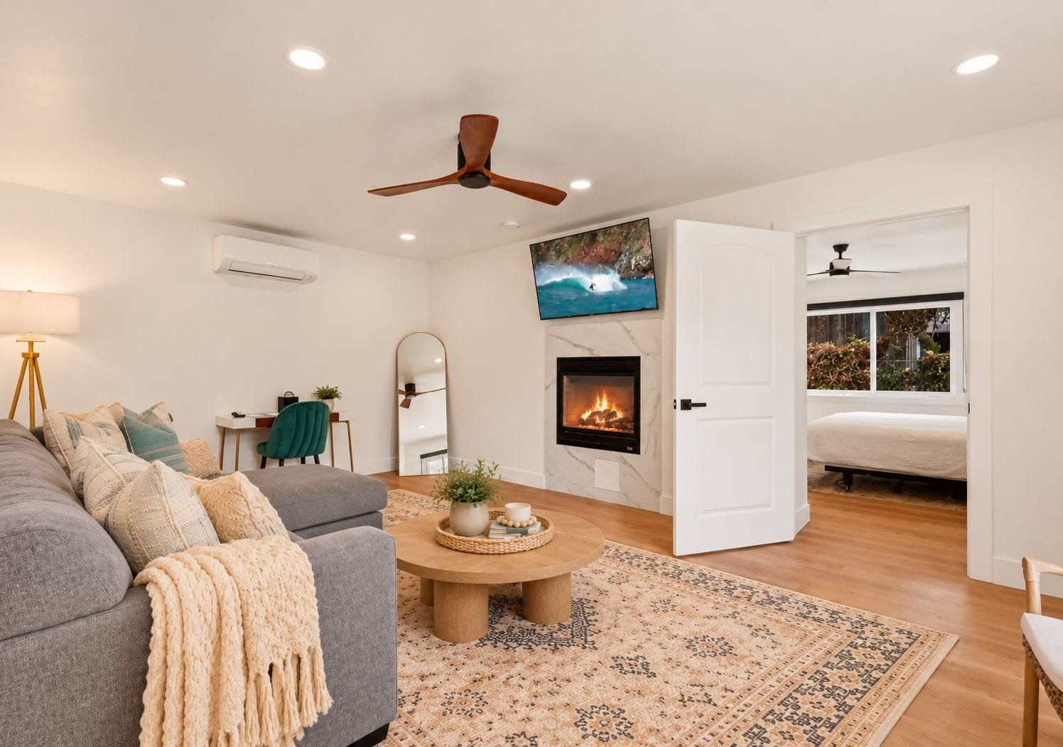 A modern living room with a fireplace, a ceiling fan, and a large TV mounted on the wall.