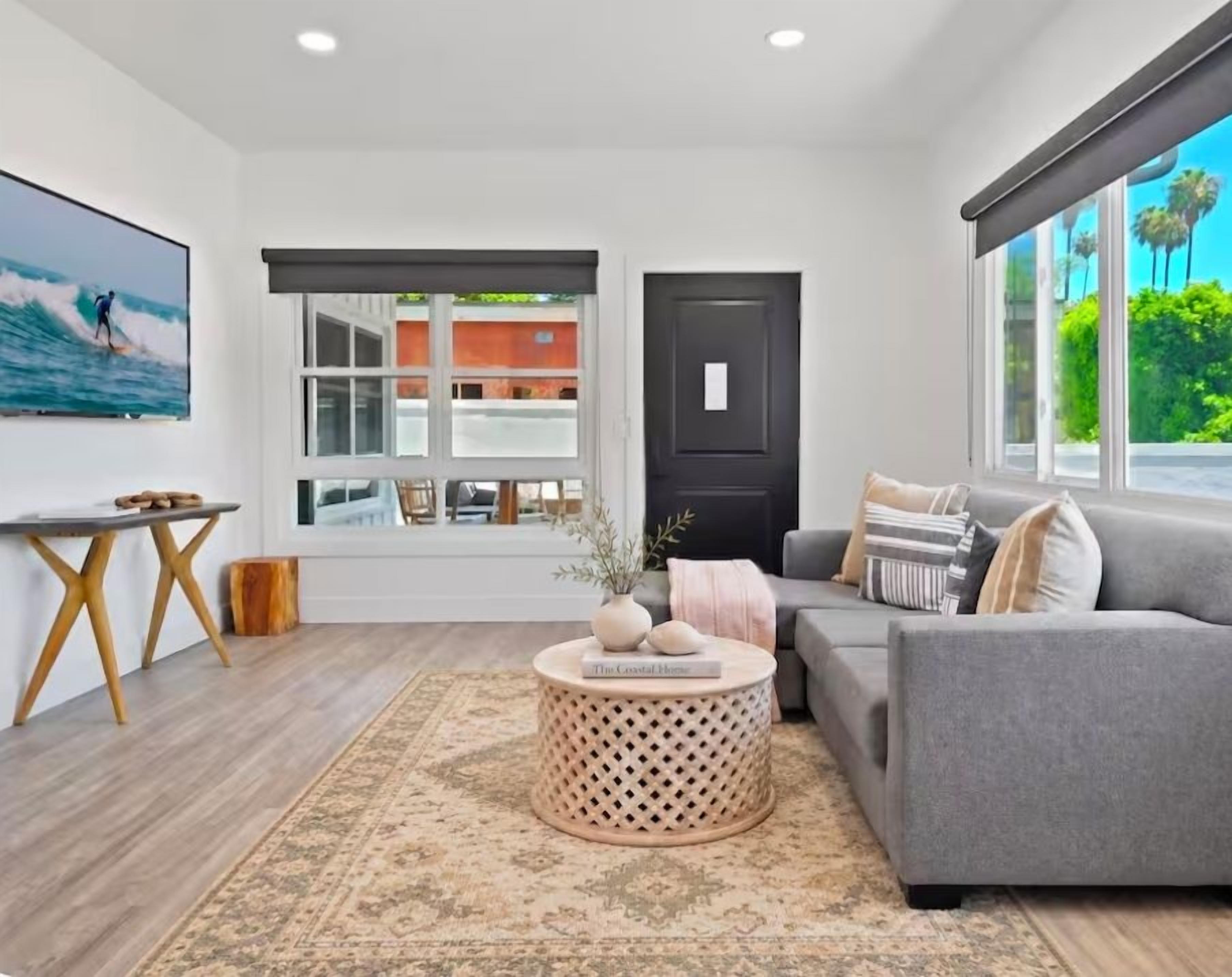 A modern living room with a grey sofa, a round wooden coffee table, and a large window with a view of palm trees.