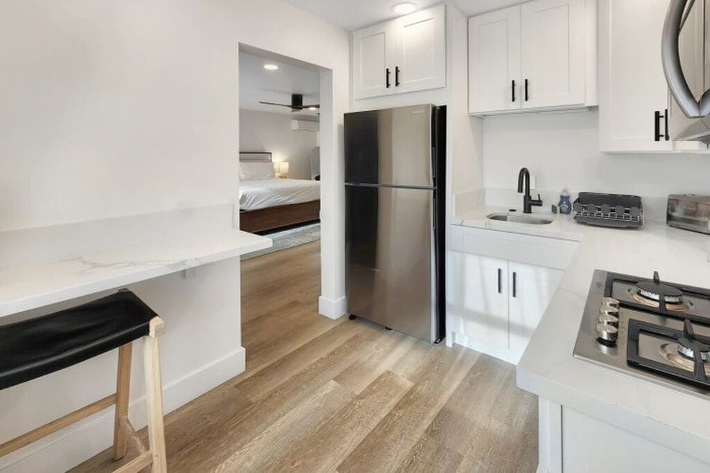 A compact kitchen with white cabinets, a stainless steel refrigerator, a gas stove, and a small countertop.