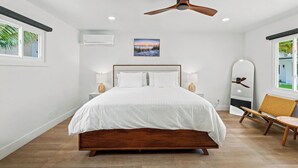 Un dormitorio con una cama de madera, un ventilador de techo, aire acondicionado de pared, un cuadro y una ventana con vistas.