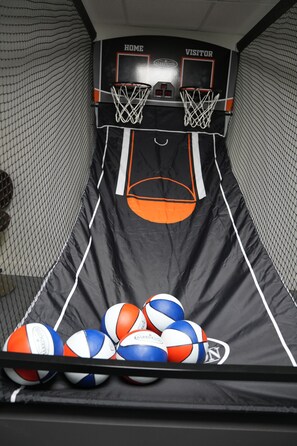 A basketball court with two hoops, labeled 'HOME' and 'VISITOR,' and a pile of volleyballs at the bottom.