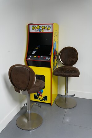 Pac-Man-peliautomaatti kahden ruskean tuolin vieressä. Tuoleissa on metallijalat.
