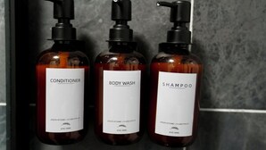 Three bottles of personal care products with pumps, labeled conditioner, body wash, and shampoo, against a tiled wall. - Cozy 2 bedroom Apartment with Arcade & Games (Cincinnatus)