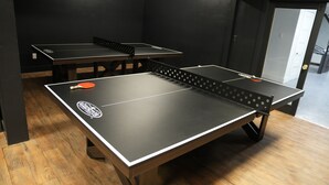 A room with ping pong tables, wooden flooring, and a door leading to another area. - Cozy 2 bedroom Apartment with Arcade & Games (Cincinnatus)