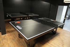 Una habitación con mesas de ping pong, piso de madera y una puerta que da a otra zona.