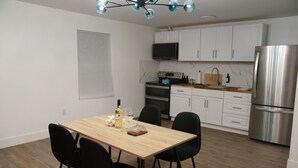 A modern kitchen with white cabinets, a stainless steel refrigerator, and a dining area with a wooden table and black chairs. - Cozy 2 bedroom Apartment with Arcade & Games (Cincinnatus)