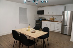 A modern kitchen with white cabinets, a stainless steel refrigerator, and a dining area with a wooden table and black chairs.