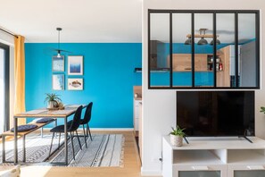 Eine moderne Küche mit Holzausstattung und schwarzem Fliesenspiegel, ein Essbereich mit Holztisch und -stühlen sowie ein Wohnbereich mit weißem Medienmöbel.