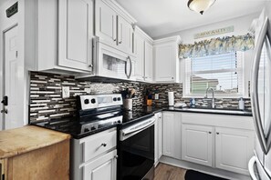 A kitchen with white cabinets, a black countertop, a microwave, an oven, and a window with blinds. - Beachfront 3BR/2BA condo in Surfside Beach that sleeps 7.  Direct Beach access (Surfside Beach)