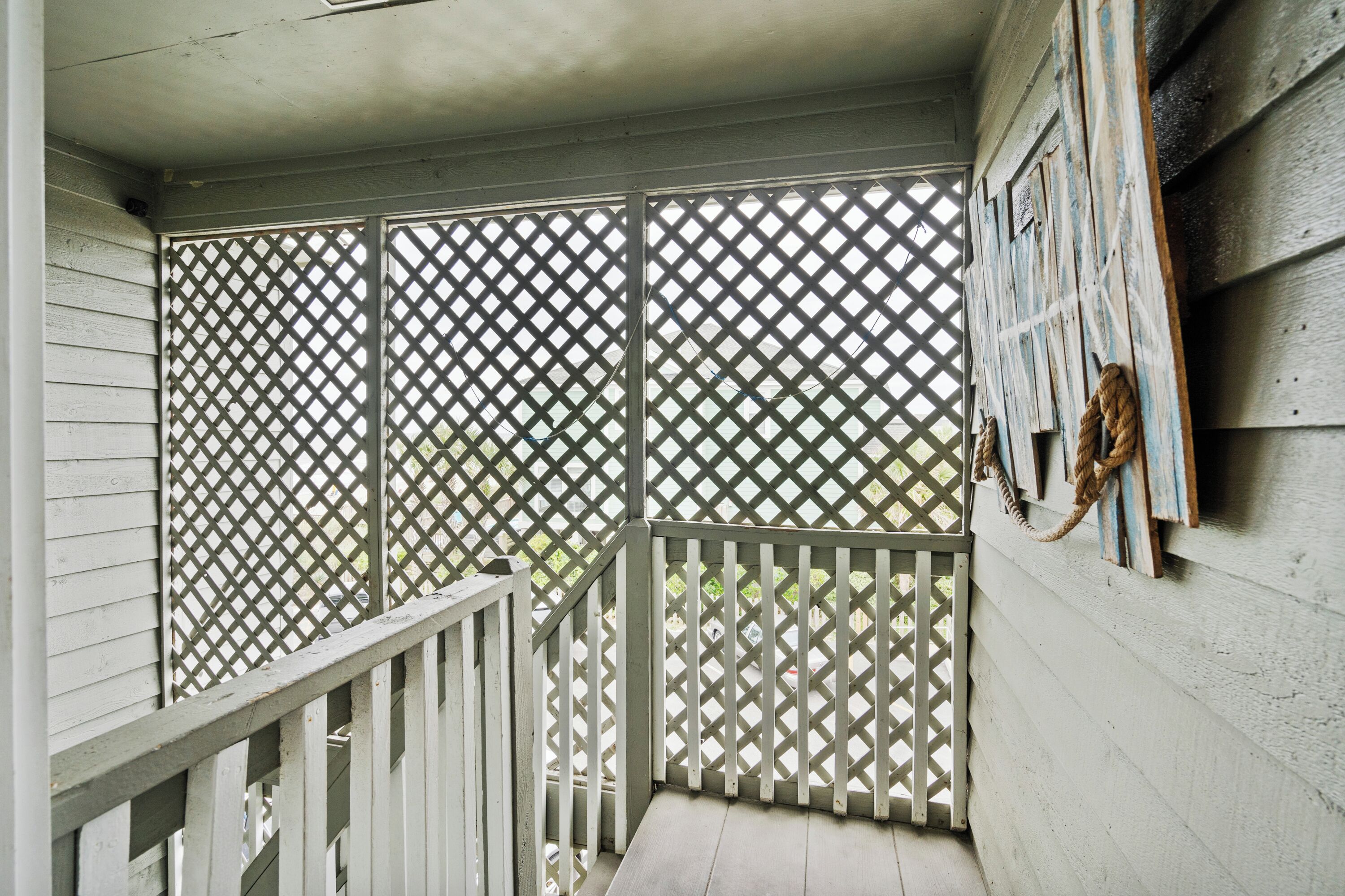 A covered porch with a lattice screen, a wooden railing, and a rope tied to the wall.