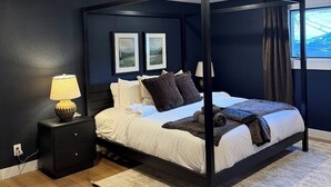 Una cama con dosel de estructura oscura, una mesita de noche con lámpara y una alfombra sobre suelo de madera.