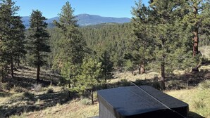 Una cabaña con una plataforma de hormigón, un banco y vistas a un bosque y montañas.