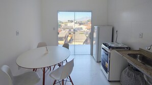 Una pequeña cocina con una mesa y sillas, un refrigerador y vista de la ciudad a través de un ventanal.