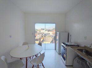 Une petite cuisine équipée d’une table et de chaises, d’un réfrigérateur, et offrant une vue sur la ville grâce à une porte vitrée.