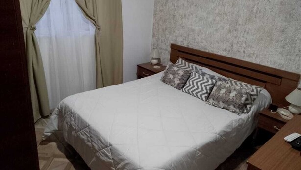 A bedroom with a bed, a nightstand, a lamp, and a window with curtains.