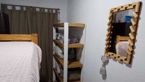 A bedroom with a bed, a wooden shelf unit, a mirror, and a curtain.