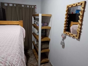 A bedroom with a bed, a wooden shelf unit, a mirror, and a curtain.