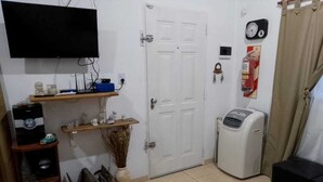 A living room with a TV, a white door, a clock, a fan, and a coffee table.