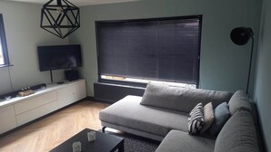 En moderne stue med en modulsofa, et fladskærms-tv, et sort sofabord og en geometrisk pendel.