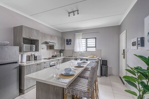 A modern kitchen with a central island, built-in appliances, and a dining area with wicker chairs. - Believe Stays 10min From Mall Ofafrica &gallagher (Johannesburg)