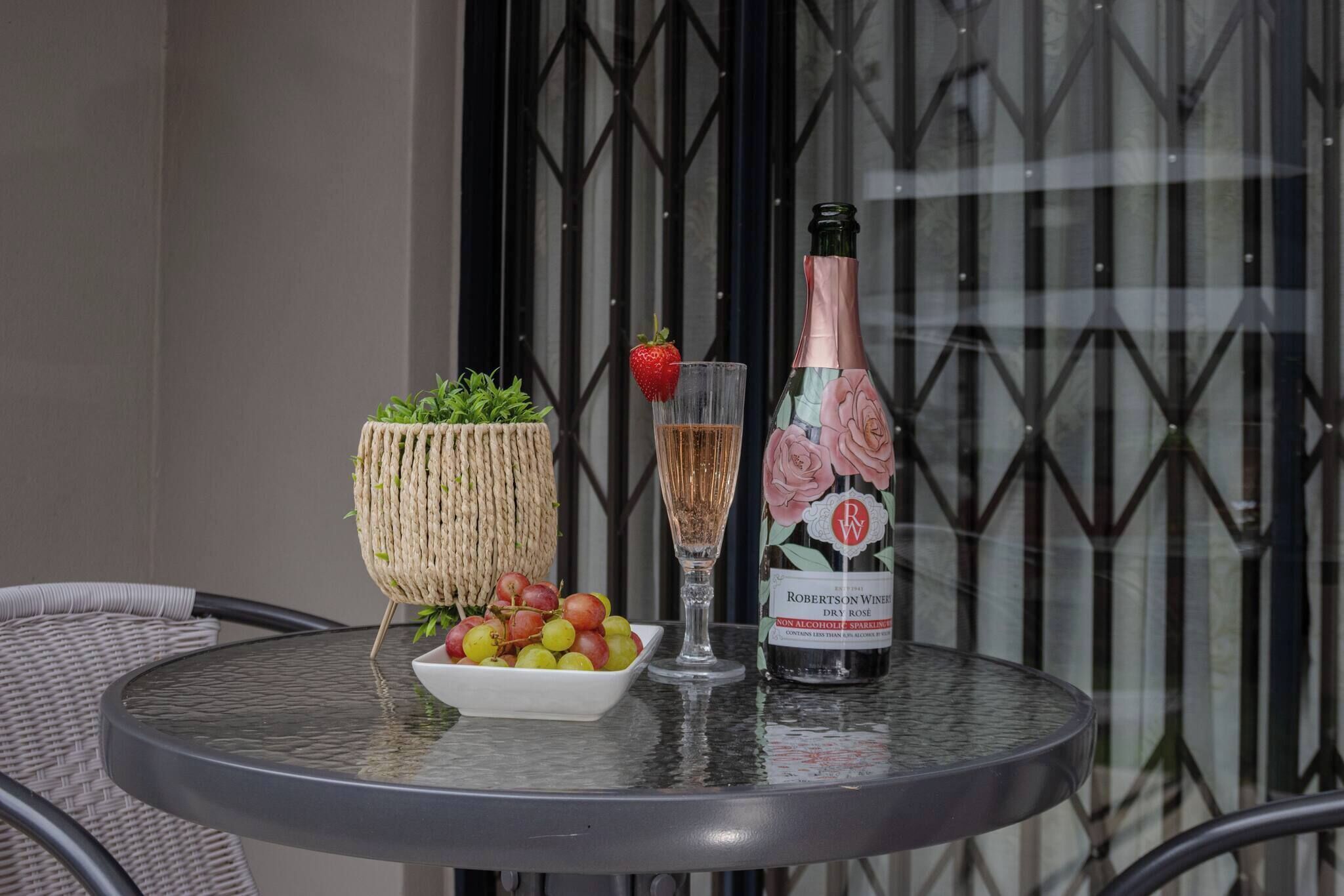 A round table with a bottle of wine, a glass, and a bowl of fruit.