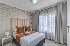 Ein Hotelzimmer mit einem Bett, einem Nachttisch, einer Lampe und einem Fenster mit Vorhängen.
