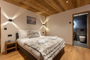 Une chambre avec un plafond en bois, un lit recouvert d’une couverture blanche et moelleuse, deux lampes fixées au mur et un tableau accroché au mur.