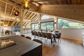 Un comedor espacioso con techo alto y ventanas amplias, vigas de madera y mobiliario moderno.