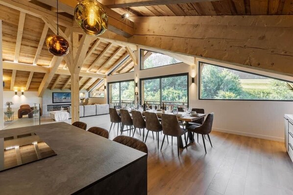 Une salle à manger spacieuse avec un plafond haut et de grandes fenêtres, des poutres en bois et un mobilier moderne.