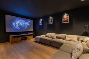 A dark-themed living room with a large flat-screen TV, a beige sofa, and framed artwork on the wall. - Chalet des Granges • 12 Guests • Spa & Private Cinema (Morzine)
