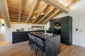 A modern kitchen with a central island, bar stools, and built-in appliances. - Chalet des Granges • 12 Guests • Spa & Private Cinema (Morzine)