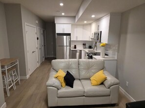 A modern kitchen with white cabinets, stainless steel appliances, and a white sofa with yellow cushions. - Spacious and Modern 2-bedroom Apartment in Calgary (Calgary)