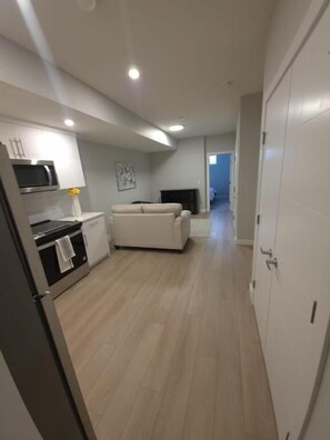 A modern kitchen with a microwave, stove, and cabinets, a white sofa, and a hallway leading to a door. - Spacious and Modern 2-bedroom Apartment in Calgary (Calgary)