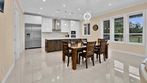 A modern kitchen with white cabinets, stainless steel appliances, and a dining area with a wooden table and chairs. - Luxury Mountain-View Estate on 1.8 Acres | Near Golden Ears Park & Hwy 1 (Maple Ridge)