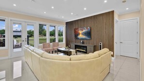 A living room with a sectional sofa, a fireplace, a TV mounted on the wall, and a view of the outdoors through large windows. - Luxury Mountain-View Estate on 1.8 Acres | Near Golden Ears Park & Hwy 1 (Maple Ridge)