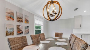 Een eetruimte met een lange houten tafel, geweven stoelen en een kroonluchter.