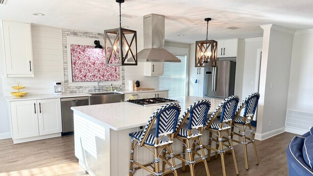 Een moderne keuken met witte kasten, een groot eiland en barstoelen.