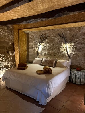 A bedroom with a stone wall, a bed with white bedding, a wooden headboard, and a small table with a telephone.