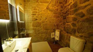 Un baño con pared de piedra, lavamanos, inodoro y zona de ducha.