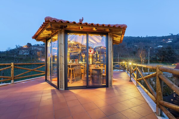 A glass-enclosed structure with a wooden roof, a wooden fence, and a view of a bar area with wooden furniture.