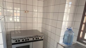 Una cocina con paredes de azulejos blancos, una estufa y un dispensador de agua grande.
