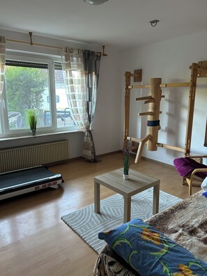 Una habitación con una cinta de correr, una pequeña mesa con una planta, una colchoneta de yoga y un rodillo de yoga.